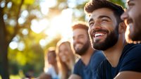 Young diverse group of friends laughing together outdoors in sunlight, expressing genuine joy and connection during social gathering. Natural bokeh background.