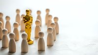 Golden award statue standing out among wooden figures representing leadership excellence and recognition in business competition.