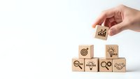 Hand placing wooden cube with growth chart icon completing business strategy pyramid on white background for corporate planning and development concepts.
