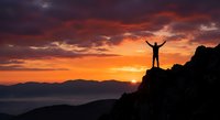 Silhouette of person with raised arms celebrating success on mountain peak at dramatic sunset with orange and purple sky over valley landscape.