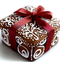 Brown gingerbread gift box decorated with white royal icing swirl pattern and red satin ribbon bow, festive Christmas holiday present on white background.