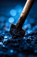 Wooden handle shovel digging dark soil against blue bokeh background, dramatic close-up photography with shallow depth of field and moody lighting effects.