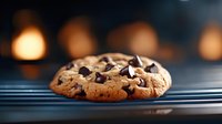 Chocolate chip cookie with melted chips on striped surface, warm bokeh lights in background, fresh baked treat for bakery, dessert, and food photography projects.