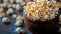 Fresh popcorn in rustic wooden bowl against dark background, selective focus on fluffy white kernels with warm lighting for cinema and snack concepts.