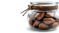 Whole nutmeg seeds in glass jar with rustic twine decoration on white background, perfect for cooking, baking, and natural food photography.