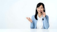 Friendly Asian businesswoman customer service representative with headset gesturing while speaking, professional support agent in blue blazer on white background.