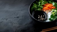 Fresh Asian salad bowl with greens, carrots and soy sauce on dark slate background. Healthy vegetarian meal with chopsticks for restaurant menu design.