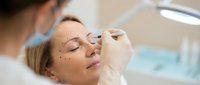 Plastic surgeon marking facial areas on relaxed Caucasian woman before cosmetic procedure in modern medical clinic for beauty enhancement surgery.