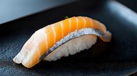 Fresh salmon nigiri sushi piece on black plate with textured rice and glossy fish slice, showcasing traditional Japanese culinary artistry in dramatic lighting.