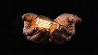 Hands gently holding glowing vintage Edison bulb against dark background symbolizing innovation, creativity and bright ideas for business concepts.
