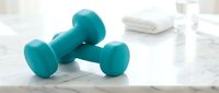 Pair of turquoise dumbbells on marble surface with towels and wellness items, representing fitness, strength training, and home gym equipment for health-conscious individuals.