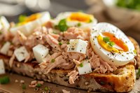 Open-faced sandwich with flaked tuna, soft boiled egg, diced mozzarella and fresh herbs on toasted artisanal bread, macro food photography with selective focus.