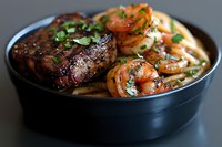 Grilled steak and sauteed shrimp served in black bowl with fresh herbs and vegetables, surf and turf dinner combination featuring juicy meat and seafood.