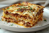 Traditional layered lasagna with meat sauce and melted cheese garnished with fresh herbs on white plate, close up view showing distinct pasta layers and rich filling.