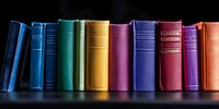 Row of colorful hardcover books standing on dark shelf against black background, spines showing various sizes and textures in rainbow arrangement.