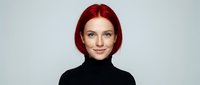 Young redhead woman with bob haircut wearing black turtleneck sweater smiling at camera against neutral background for professional headshot photography.