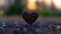 Heart-shaped soil or coffee grounds on blurred natural background with sunset bokeh, shallow depth of field macro photography creates romantic mood.