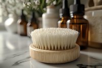 Eco-friendly bamboo body brush with natural bristles on marble counter, amber glass bottles and flowers in soft morning light for wellness spa concept.