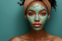 Young African American woman with curly hair wearing turquoise clay face mask for skincare routine and spa treatment on matching teal background.