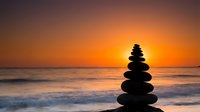 Zen stone stack balanced on beach at sunset with golden sky and ocean waves creating peaceful meditation atmosphere for wellness and mindfulness concepts.