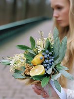 Young blonde woman holding rustic wedding bouquet with lemons, berries and eucalyptus leaves for bridal ceremony and floral arrangements.