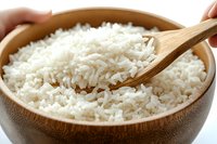 Steamed white jasmine rice served in wooden bowl with bamboo spoon, close up view showing fluffy texture and individual grains in natural lighting.