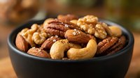 Mixed nuts assortment in black bowl featuring walnuts, almonds, cashews and pecans for healthy snacking and cooking ingredients.