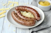 Grilled bratwurst sausages served with sauerkraut and mustard sauce on white plate. Traditional German cuisine on rustic wooden table with napkin and condiments.