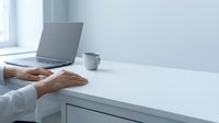 Professional woman hands typing on laptop computer at modern white desk workspace with coffee cup in bright office environment for business productivity.