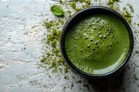 Fresh matcha green tea powder in ceramic bowl with foam bubbles on white textured surface, traditional Japanese tea ceremony preparation for wellness drinks.