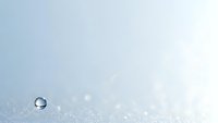 Single water droplet on pristine white snow surface with soft bokeh light effects creating minimalist winter composition for seasonal designs.