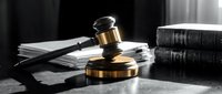 Wooden gavel with brass band on dark surface beside legal books and documents in dramatic lighting for courtroom and justice concepts.