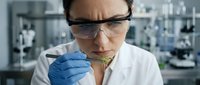 Female scientist in safety glasses examining plant sample with tweezers in modern laboratory for botanical research and genetic analysis.