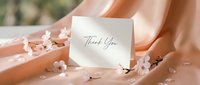 Thank you card with elegant script lettering on peach silk fabric, surrounded by delicate cherry blossoms, soft romantic styling for weddings and events.