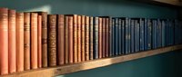 Row of vintage leather-bound books on wooden shelf creating gradient from warm orange to cool blue tones for library and education concepts.