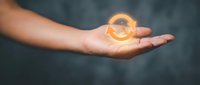 Caucasian male hand holding glowing golden orb with light energy effect against dark background, representing power, innovation, and future technology concepts.