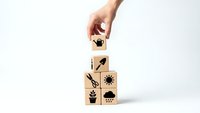 Hand placing wooden cube with lightbulb icon on stack of blocks featuring business growth symbols on white background for creative concepts.