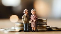 Elderly couple figurines standing on stacked coins representing retirement savings, pension planning, financial security and investment growth for senior citizens.