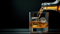 Premium whiskey pouring into glass with ice cubes on dark background. Luxury alcohol beverage concept for bar, restaurant and hospitality industry.