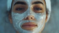Young Middle Eastern woman with clay face mask during spa skincare treatment, close up portrait showing glowing skin and natural beauty in soft lighting.