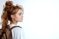 Young Caucasian woman with curly ginger hair in white shirt and brown backpack looking away in profile against light background, natural makeup and casual style.