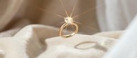 Elegant gold engagement ring with sparkling diamond creating starburst light effect on soft white silk fabric for wedding and jewelry concepts.