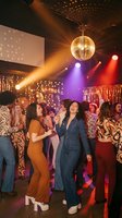 Diverse group of young women dancing and celebrating at retro disco party with mirror ball and colorful stage lights in nightclub atmosphere.