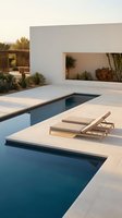 Modern minimalist pool area with geometric design featuring clean lines, white concrete deck, and contemporary lounge chairs at luxury residential home.