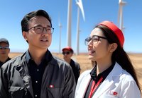 Young Asian professionals in work uniforms inspect wind turbine farm on sunny day, discussing renewable energy project against blue sky and white windmills background.