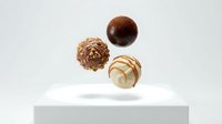 Assorted chocolate truffles and bonbons floating above white platform, featuring dark chocolate, caramel swirl, and textured varieties for confectionery, bakery, and food styling projects.