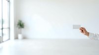 Businesswoman in white shirt holding blank business card in modern minimalist office space with natural light and potted plant for corporate branding.