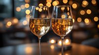 Two elegant wine glasses filled with golden sparkling wine against blurred warm bokeh lights background, romantic celebration atmosphere for luxury dining.