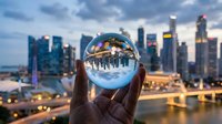 Hands holding crystal ball reflecting cityscape skyline at sunset, urban landscape photography for business, travel, and vision concepts.