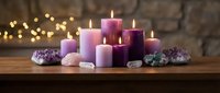 Purple candles of various sizes burning on wooden surface with amethyst crystals and warm bokeh lights creating peaceful spa atmosphere for relaxation.
